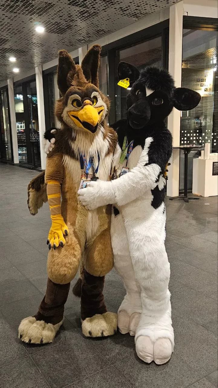 Two fursuiters (an owl-style character and a Holstein cow-style character) posing together in the Malmö Mässan venue lobby at NordicFuzzCon 2026.