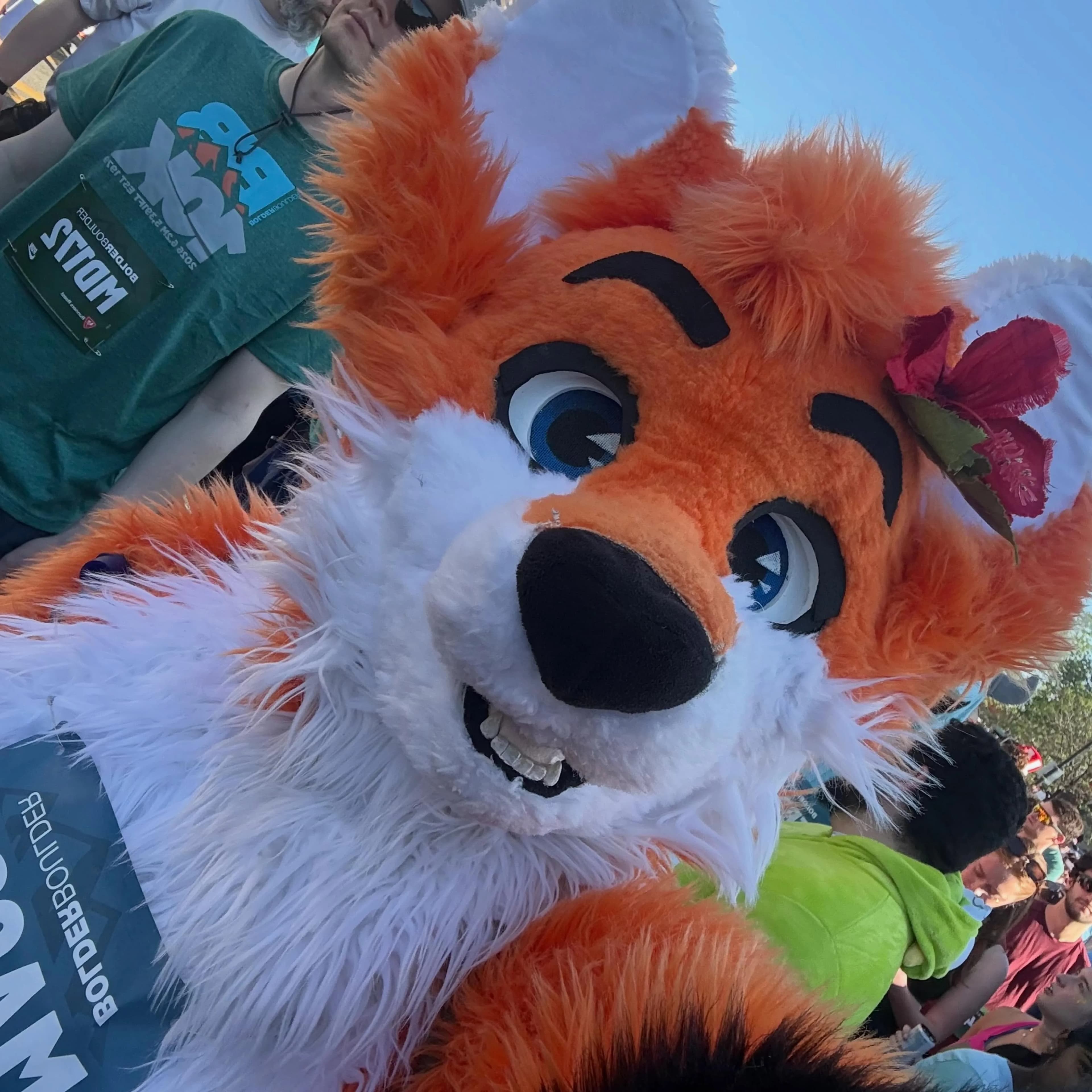 Close-up selfie of Blaze the Foxx with another finisher in a teal BolderBoulder t-shirt, the MA290 bib upside-down in frame as the camera tilts.
